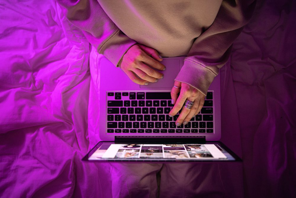 Mãos digitando em um notebook sob luz roxa